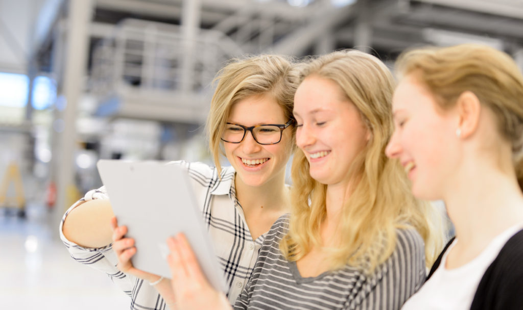 Drei Schülerinnen schauen auf ein Tablet.